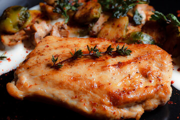 Pork neck steak with vegetables and grilled mushrooms on a black plate. Spices - ground pepper, parsley, basil, thyme, white garlic sauce. Detailed texture of fried meat.