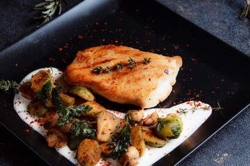 Pork neck steak with vegetables and grilled mushrooms on a black plate. Spices - ground pepper, parsley, basil, thyme, white garlic sauce. Detailed texture of fried meat.