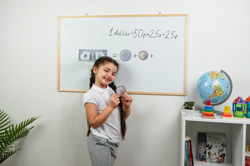Little girl stands near a white board, smiles and shows how she successfully solves mathematical...