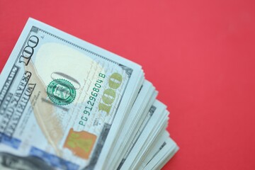 Big amount of hundred dollar bills in thick stack lies on bright red color paper background