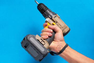 Man hand holds cordless screwdriver on blue background.