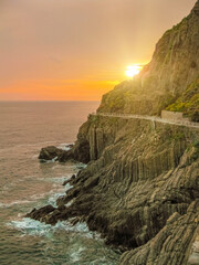 sunset on the rocky cliffs of the Italian riviera coastline as the sun sets over the ligurian sea. Tourists enjoy view walking along the famous path of love at sunset in Cinque Terre National park