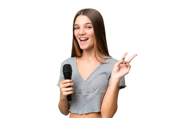 Teenager singer girl picking up a microphone over isolated background smiling and showing victory...