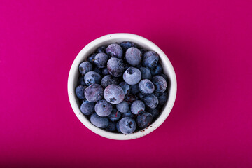 blueberries in a white bowl on a pink background