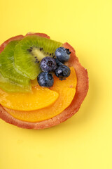 shortbread basket cake with cream, blueberries, peaches and kiwi on a plate on a yellow background