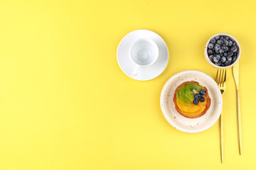 shortbread basket cake with cream, blueberries, peaches and kiwi on a plate on a yellow background