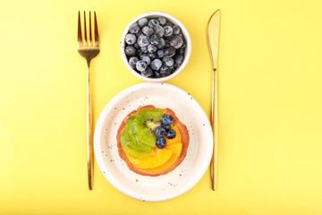 shortbread basket cake with cream, blueberries, peaches and kiwi on a plate on a yellow background