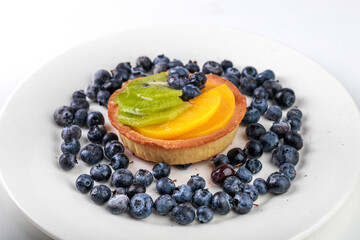 shortbread basket cake with cream, blueberries, peaches and kiwi on a plate on a white background