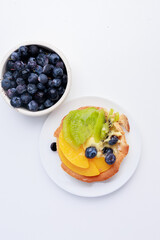 shortbread basket cake with cream, blueberries, peaches and kiwi on a plate on a white background