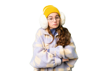 Teenager girl wearing winter muffs over isolated chroma key background making doubts gesture while lifting the shoulders