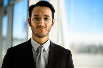 Fototapeta premium Professional businessman in a black suit with glasses and focused expression in a modern office setting, exuding leadership, confidence, and corporate business vibes
