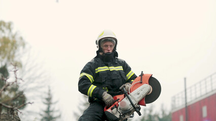 A firefighter works in extreme conditions, wearing protective clothing and a helmet, demonstrating professionalism and precision. A fireman cuts metal with a special tool, causing a powerful stream of