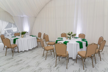 Wine glasses, silver tableware and green napkins on round tables covered with white tablecloth.