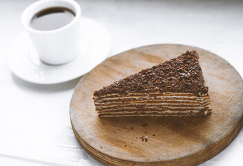 Piece of chocolate cake on a wooden plate with a cup of coffee