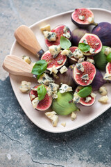 Fresh fig fruits with blue cheese and basil, vertical shot on a grey and beige granite background, middle close-up, selective focus
