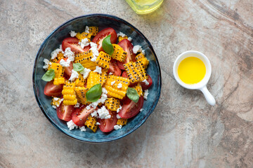 Blue bowl with tomato and grilled corn salad, flat lay on a brown granite background, horizontal shot