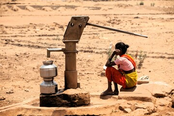 Tribal woman waiting near hand pump for water, India