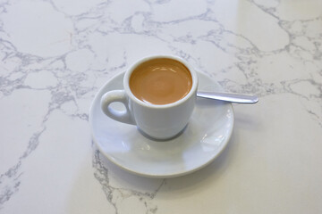 A classic espresso served in a white ceramic cup on a matching saucer. The rich coffee contrasts beautifully with the marble surface, capturing the essence of a simple, elegant coffee moment