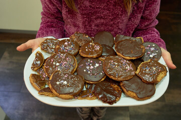 Child holding with her hands a white tray full of homemade chocolate covered cookies decorated with...