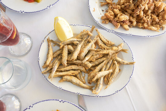 Top view of traditional Spanish fried fish dishes like whitebait or small anchovies with fresh lemon wedges, ready to share on a white tablecloth setting