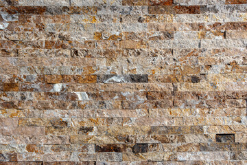 Wall made of stacked stone tiles in various shades of brown, beige, gray, and white. The stones are...