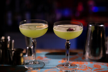 Glass of gin based Basil Smash cocktail on bar. Two cocktails of gin. Blurry background. Basil smash alcoholic cocktail drink with dry gin, syrup, lemon, basil and ice, dark bar counter background.