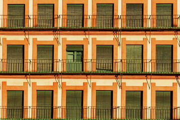 Rows of repeated windows on balconies closed with an old slat blind, except one that has the blind...