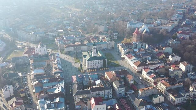 A quadcopter captures a stunning panorama of Drohobych, Ukraine, focusing on the central square where a historic town hall stands proudly. The video highlights the town's charm and rich heritage from