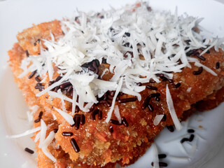 Pisang Bakar Coklat Keju or Grilled Banana Chocolate Cheese serve with chocolate sprinkles and cheddar cheese graters on white plate.