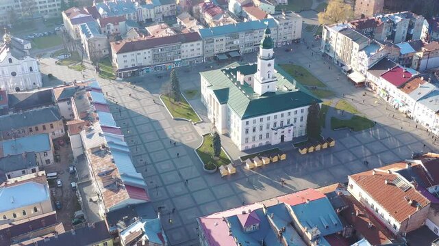 A quadcopter captures a stunning panorama of Drohobych, Ukraine, focusing on the central square where a historic town hall stands proudly. The video highlights the town's charm and rich heritage from