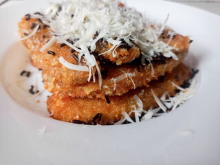 Pisang Bakar Coklat Keju or Grilled Banana Chocolate Cheese serve with chocolate sprinkles and cheddar cheese graters on white plate.