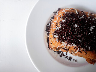 Pisang Bakar Coklat Keju or Grilled Banana Chocolate Cheese serve with chocolate sprinkles and cheddar cheese graters on white plate.