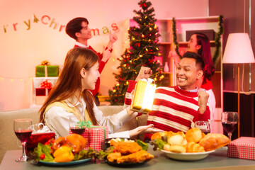 Lively New Year Eve and christmas party Asian friends and colleagues of various ages celebrating together. Champagne, wine, gift boxes, festive decorations create a warm, joyful holiday atmosphere.