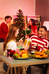 Lively New Year Eve and christmas party Asian friends and colleagues of various ages celebrating together. Champagne, wine, gift boxes, festive decorations create a warm, joyful holiday atmosphere.