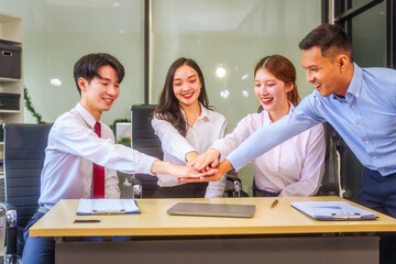 Fototapeta premium In a collaborative office setting, two men and two women, including a boss and employees, join hands and raise their hands in unity, celebrating teamwork and achieving a business target together.
