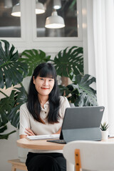 A woman sits at a desk with a laptop in a bright, plant-filled office, exuding professionalism and focus.