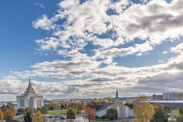 Mormon Temple in Kyiv. White stone temple. Panorama of an autumn European city. Well-groomed city park on a sunny day. Sights of Ukraine. Tourism in Ukraine. High blue sky. 