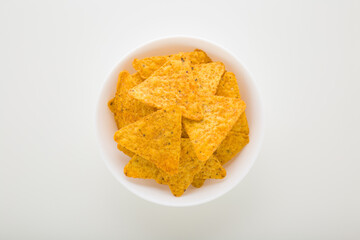 Full white bowl of yellow tortilla chips on light gray table background. Closeup. Top down view.