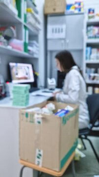 Blurred background of woman pharmacist working with medications at the table in the drugstore. Medical worker sitting in front of computer inside a pharmacy office