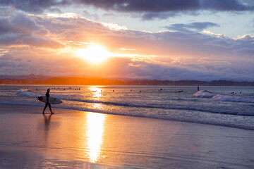 Surfer on the beach walking into the ocean with a sunset sky. Gold Coast, Australia.