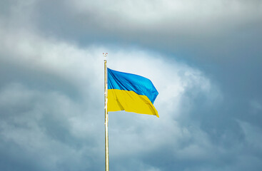 The flag of Ukraine against the background of a dark sky in windy weather.