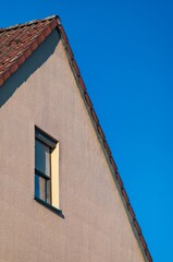 Gable end of house with clay roof tiles and window showing half-closed venetian blinds against blue sky