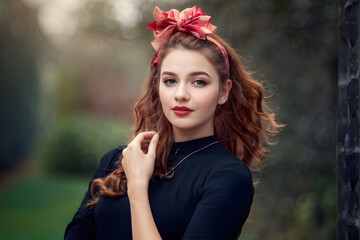A woman with red hair and a red bow in her hair poses for a photo