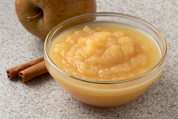 Glass bowl with organic homemade apple sauce with cinnamon and fresh apple on the background close up  