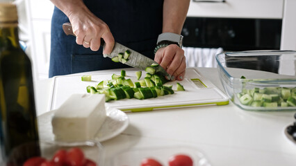 Woman At Home In Kitchen Cuts Cucumbers Preparing Greek Salad