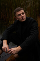 Obraz premium A European man in a black coat walks in the park near the water at dusk in autumn
