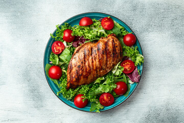 Grilled chicken breast ( fillet ) with lattuce salad and cherry tomatoes . Top view