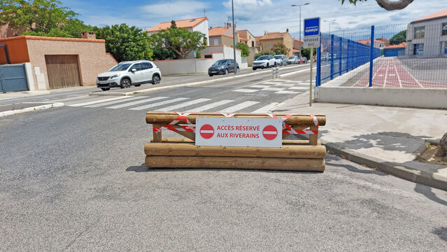 Barrière en rondins de bois portant un panneau indiquant sens interdit, accès réservé aux riverains.