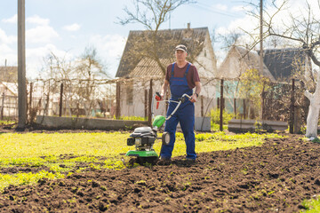 A farmer in the garden tills the land with a motorized cultivator or power tiller, preparing the...