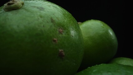 Slices of lime are meticulously arranged in a pile, set against a black background. Each lime slice is captured in stunning detail, its vibrant green hue and enticing texture. Close up. Comestible.
